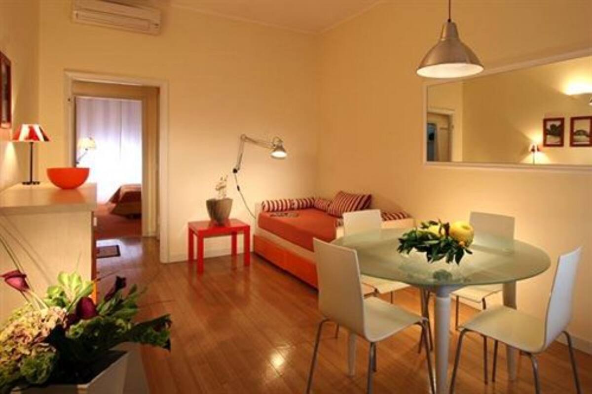 Un espace de vie compact comprenant un coin repas, un lit avec une literie rouge et une petite table sur laquelle se trouve un bol.