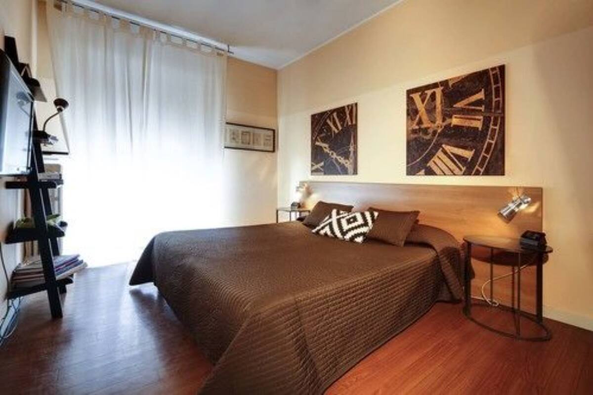 Une chambre à coucher avec un grand lit, une table de chevet, une lampe et deux horloges murales.
