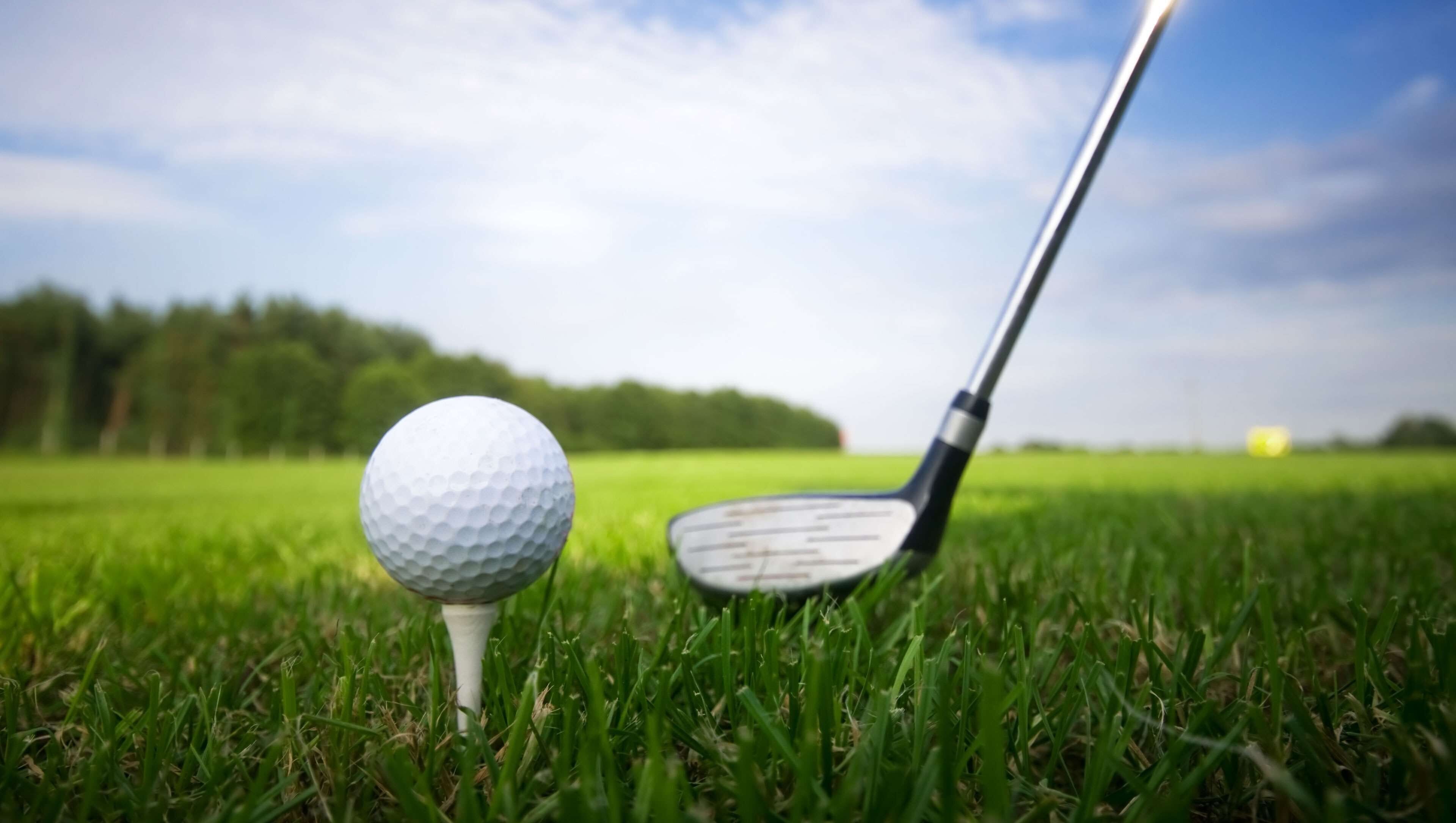 A golf ball on a tee and a golf club on a grassy field.