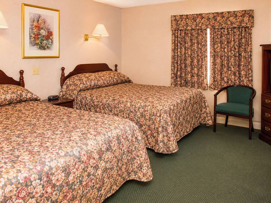A hotel room with two beds, a chair, a television, and a window with curtains.
