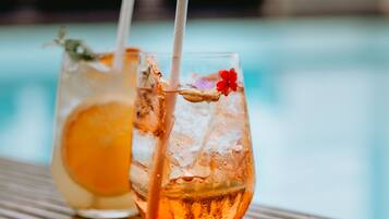 Two glasses of iced drinks with straws on a wooden table by a pool.