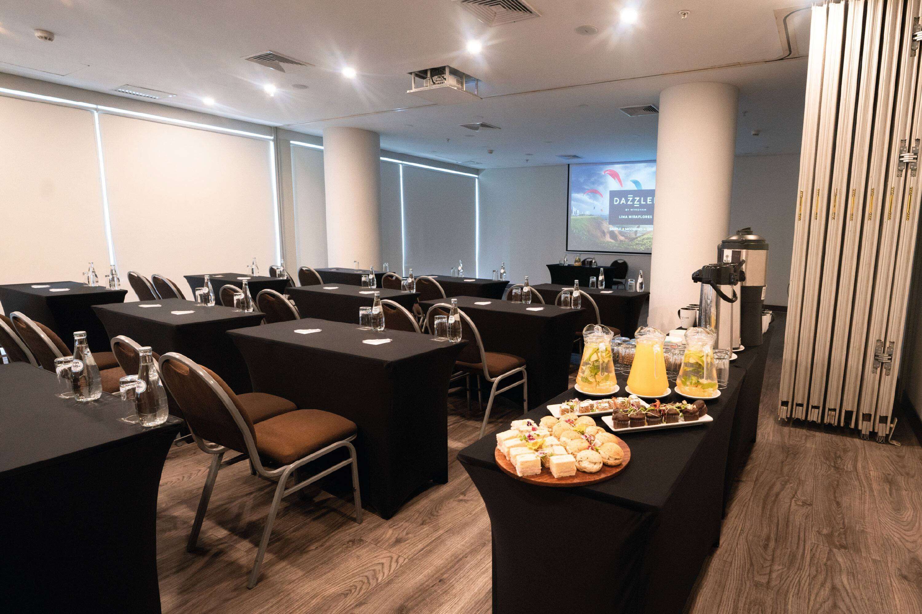 A conference room with tables, chairs, and a buffet area with food and drinks.