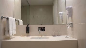 Une salle de bain moderne équipée d’un lavabo, d’un porte-serviettes, d’un miroir, d’un sèche-cheveux et d’une douche.