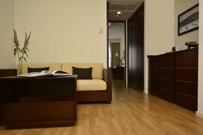 A modern living room with a wooden floor, a beige sofa, a dark brown coffee table, and a vase with flowers.