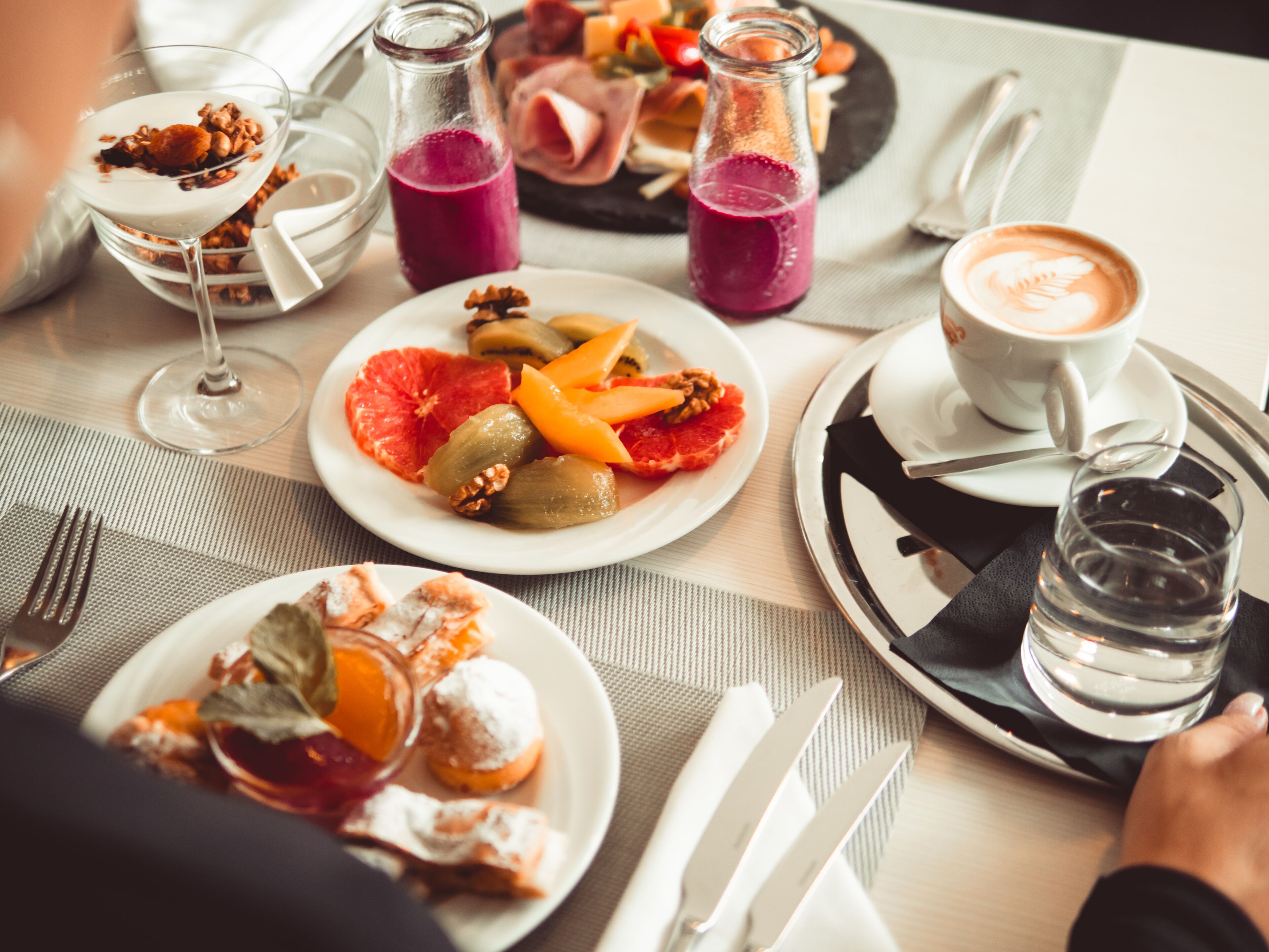 Una mesa de comedor con varios platos, incluyendo un plato con fruta y frutos secos, un vaso de jugo de uva y una taza de café.