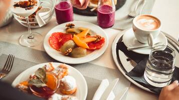 Una mesa de comedor con varios platos, incluyendo un plato con fruta y frutos secos, un vaso de jugo de uva y una taza de café.