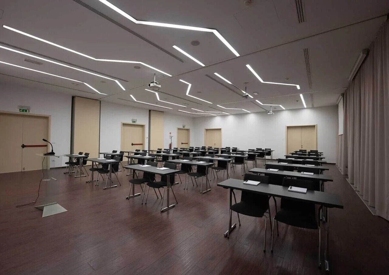 Ein Konferenzraum mit modernem Deckenstil, mehreren Tischen und Stühlen für Besprechungen.