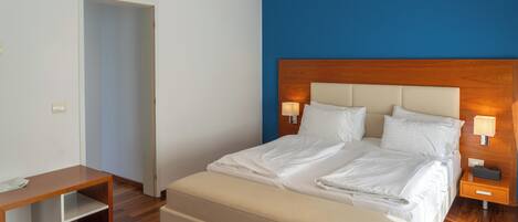 A hotel room with a bed, bedside lamps, a wooden nightstand, a small table, and a door.