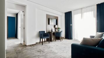 A modern hotel room with a living area, a dining space, and a large window with curtains.