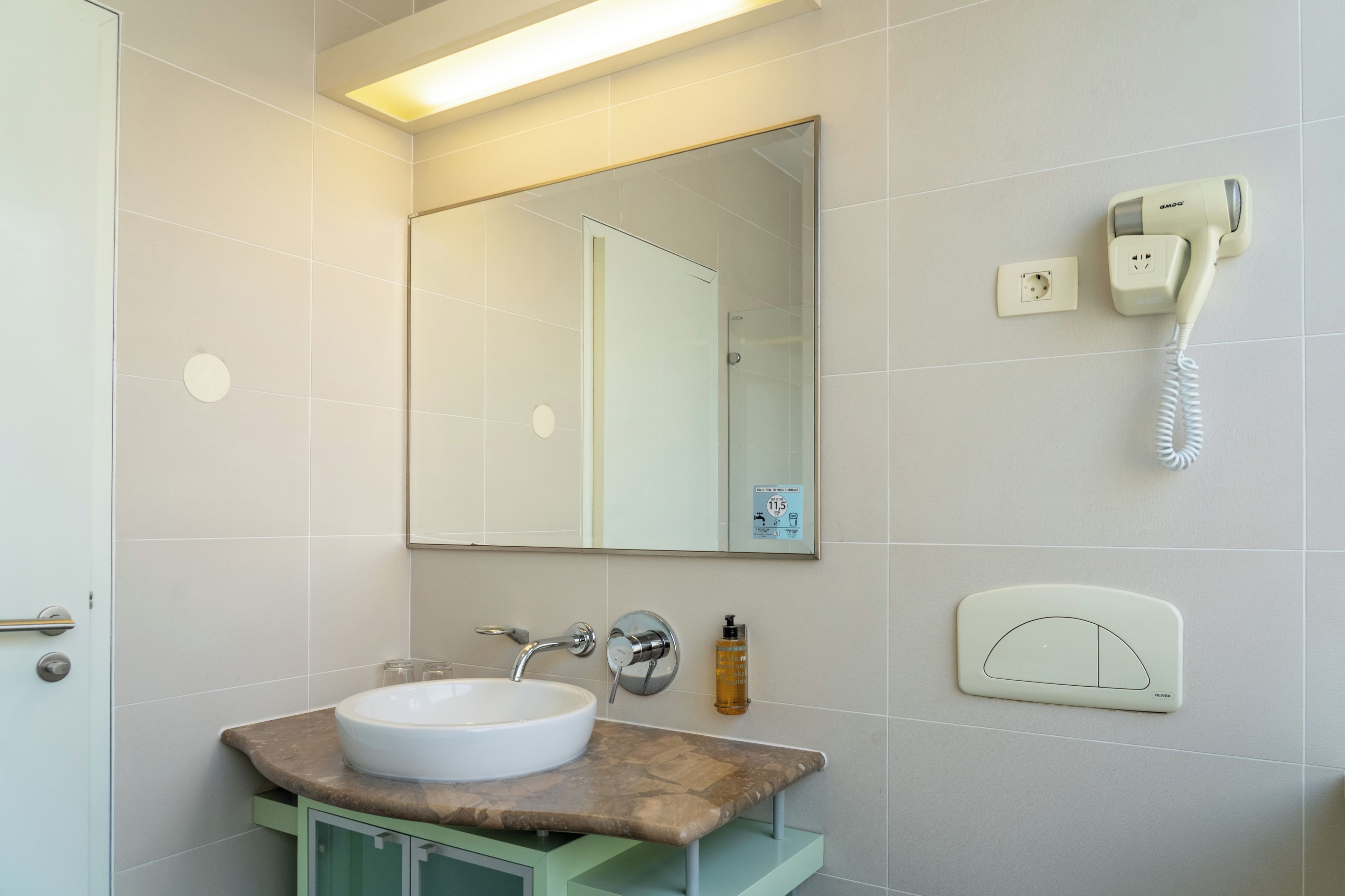 A bathroom with a white sink, a mirror, a handheld phone, and a soap dispenser.