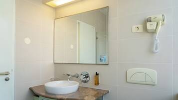 A bathroom with a white sink, a mirror, a handheld phone, and a soap dispenser.
