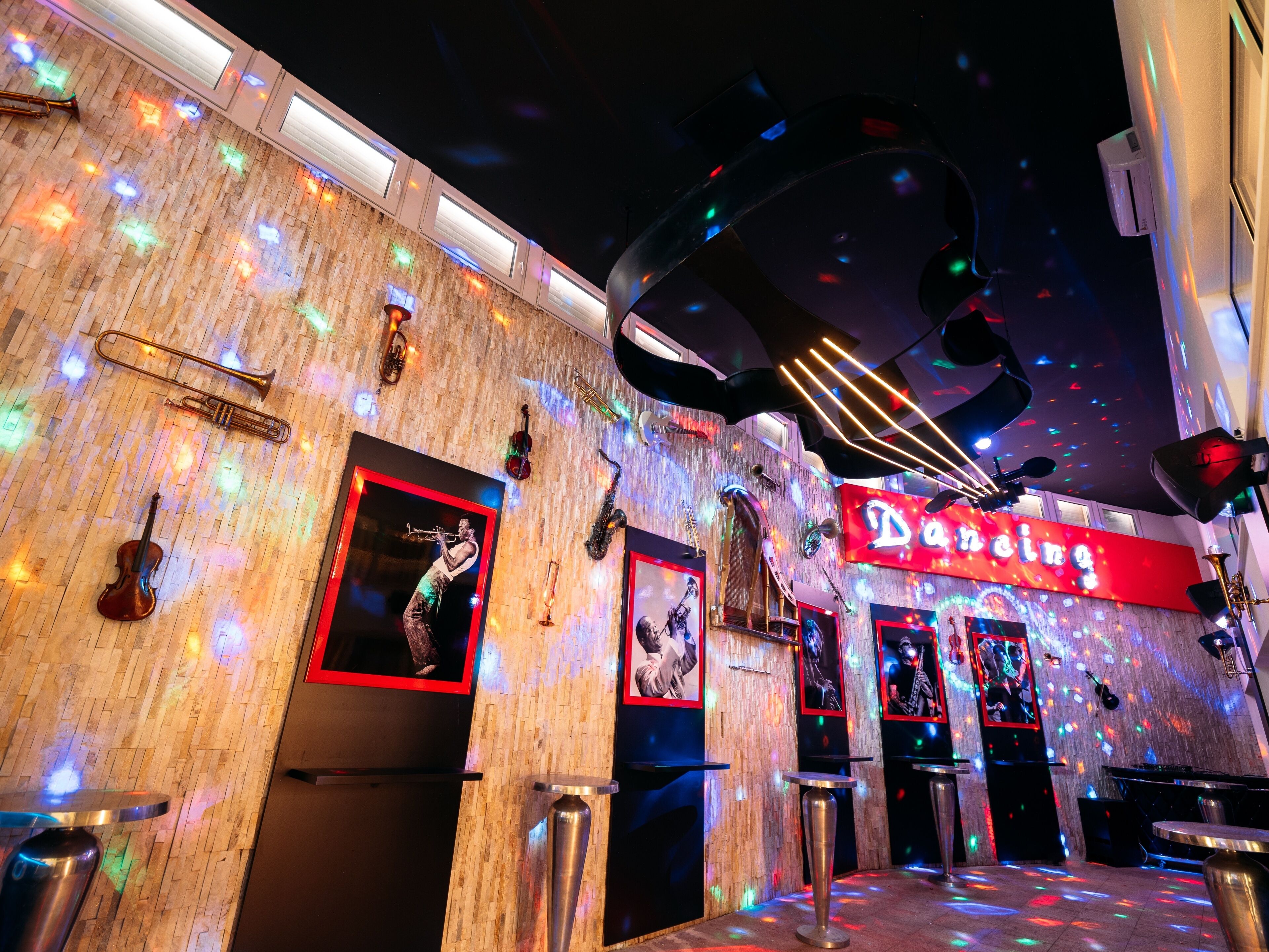 Eine Bar mit einer Holzwand, beleuchtet von bunten Lichtern, und einem Neon-Schild mit der Aufschrift 'Dancing'.
