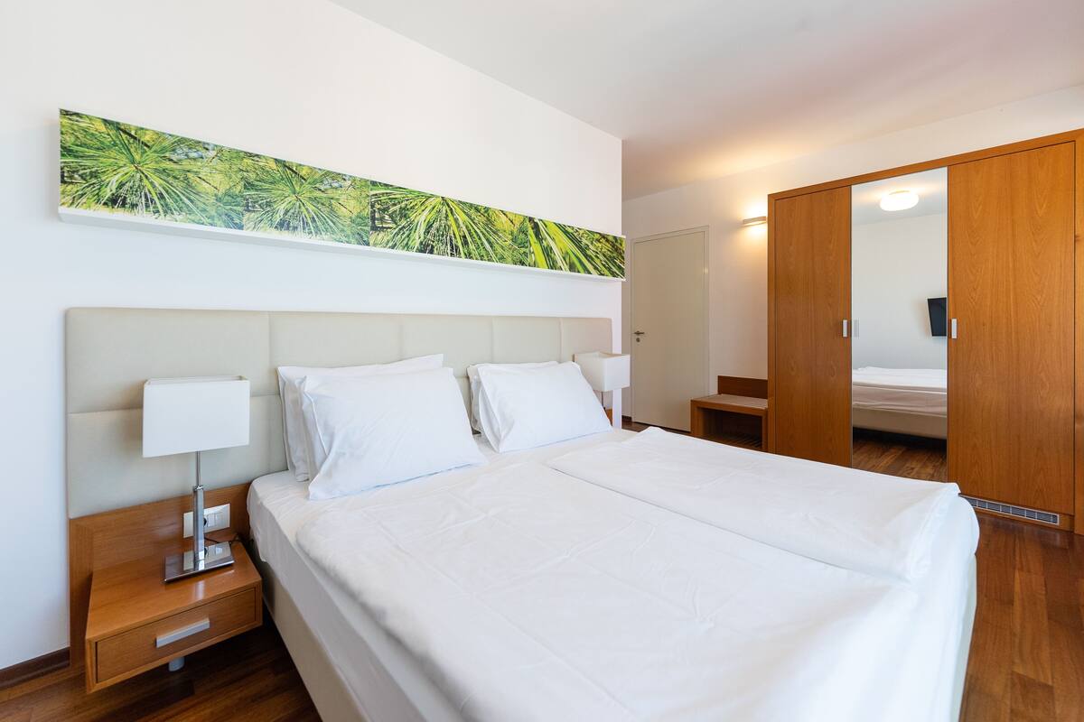 Una habitación de hotel con una cama grande, una mesita de noche con lámpara, un armario de madera y una obra de arte colgada en la pared.