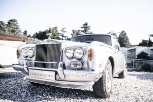 Un Rolls-Royce blanco clásico con la leyenda “EUROTAS HOTELI” en la parrilla delantera, estacionado sobre grava.