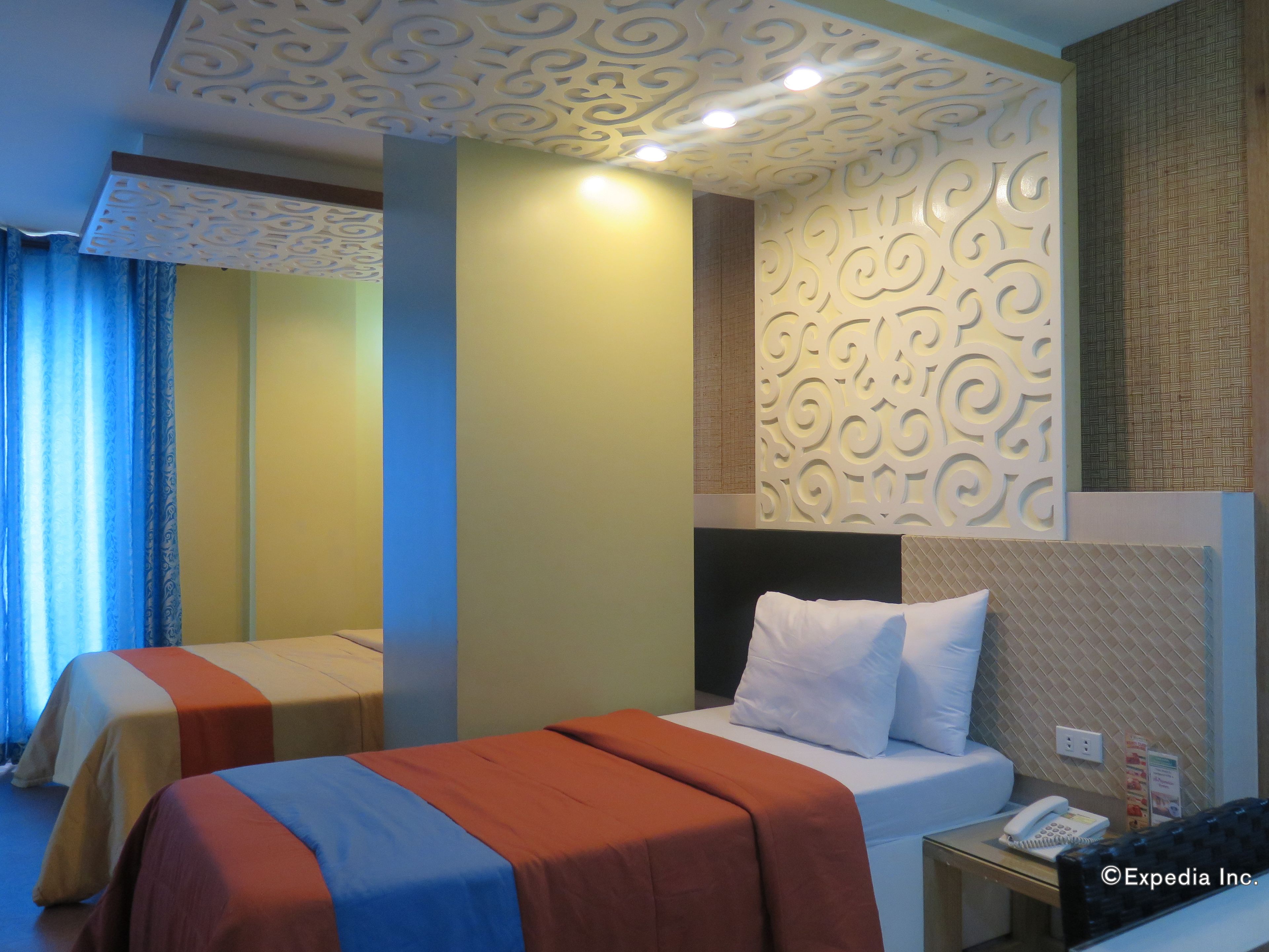 Een hotelkamer met twee bedden, een nachtkastje met telefoon en decoratieve wandpanelen.