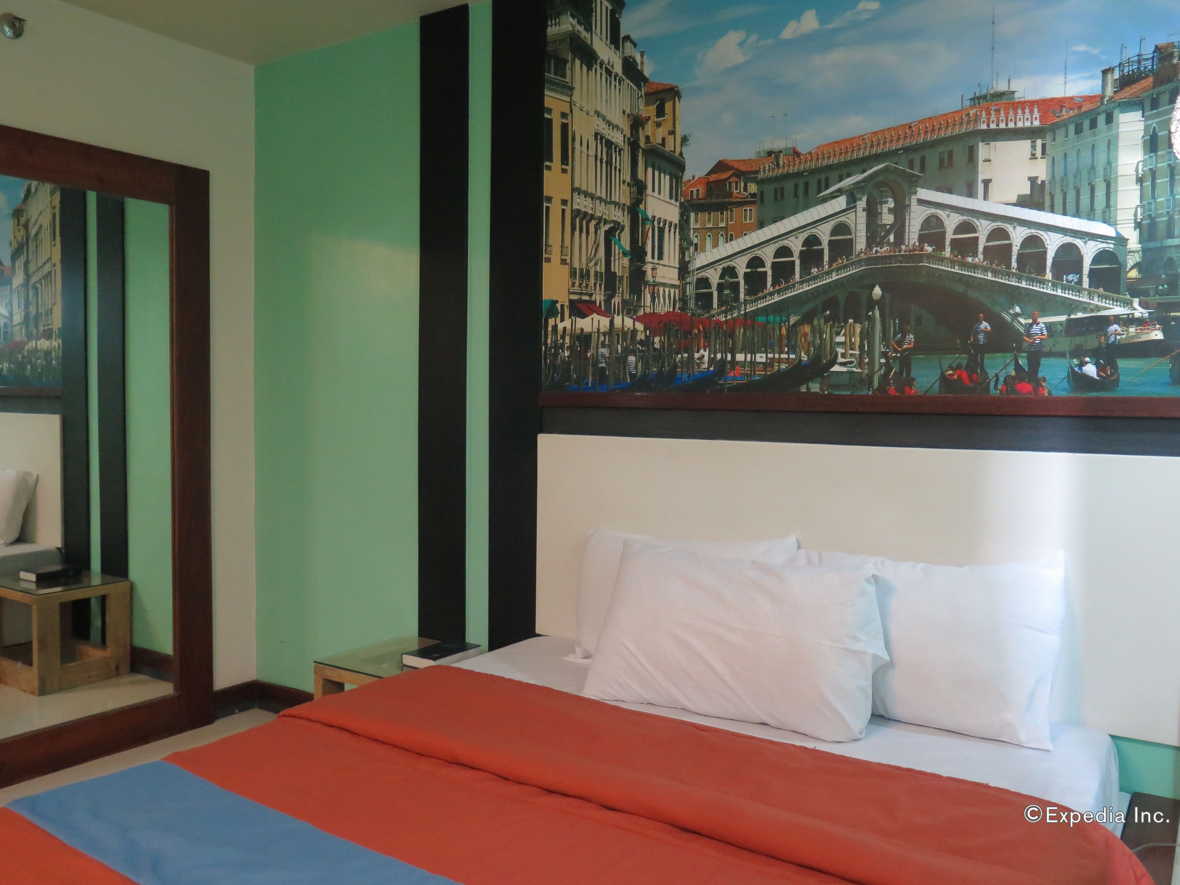 Habitación de hotel con cama, mesita de noche, una pequeña mesa y un cuadro en la pared con una vista urbana.
