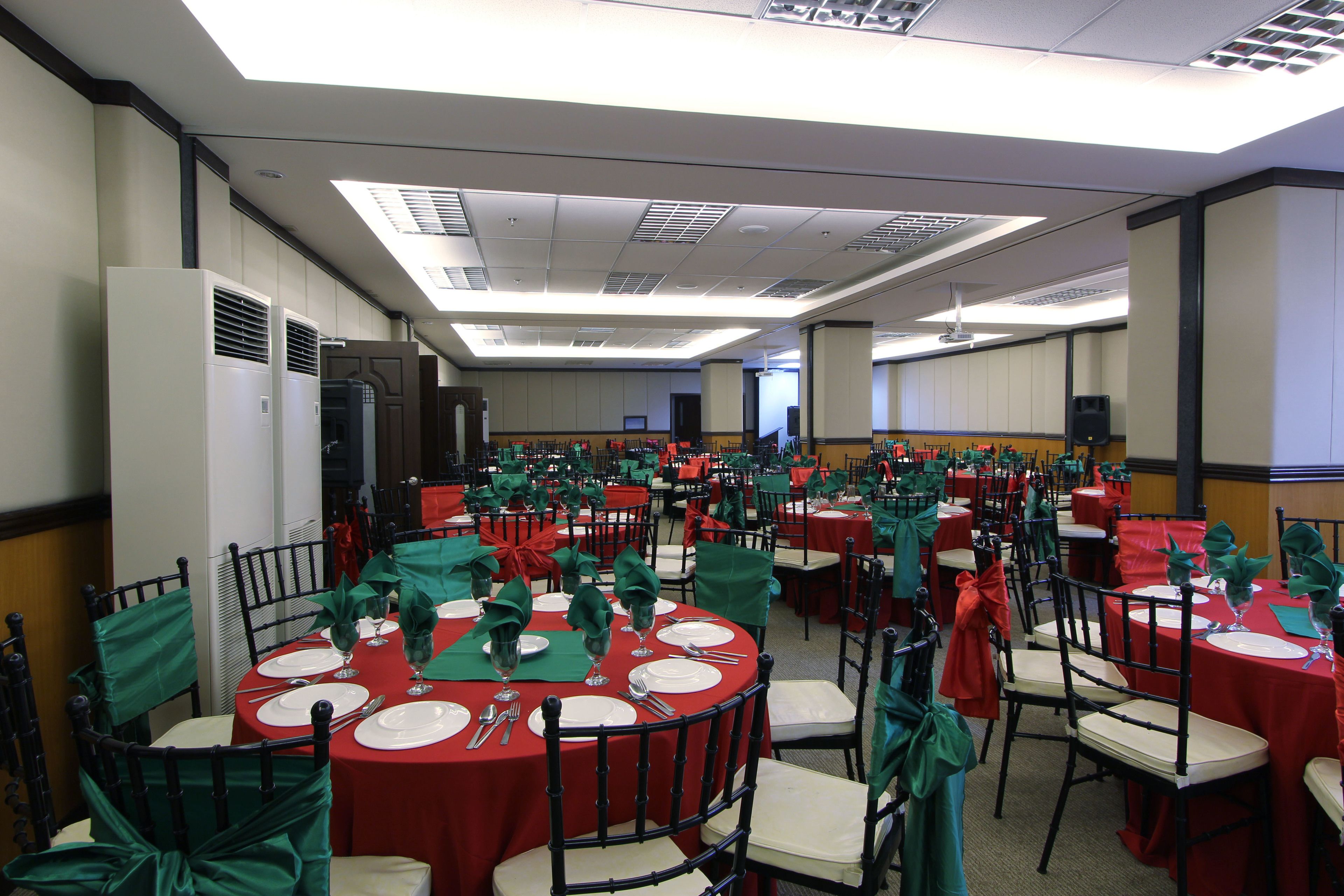 Un salón de banquetes con varias mesas redondas, cada una dispuesta con platos blancos, cubiertos y servilletas verdes.