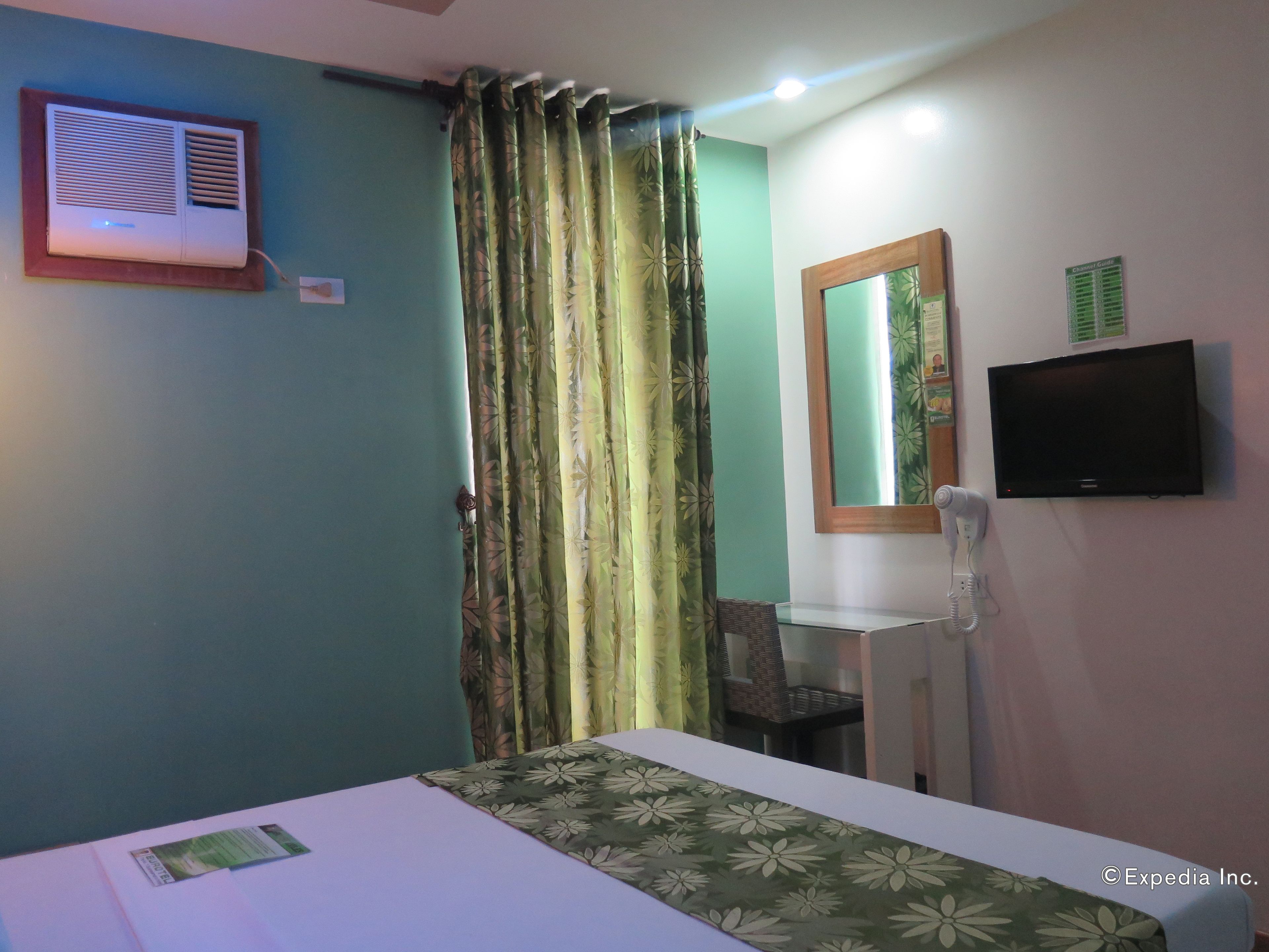A hotel room with a bed, a desk, a mirror, a TV, and a telephone.
