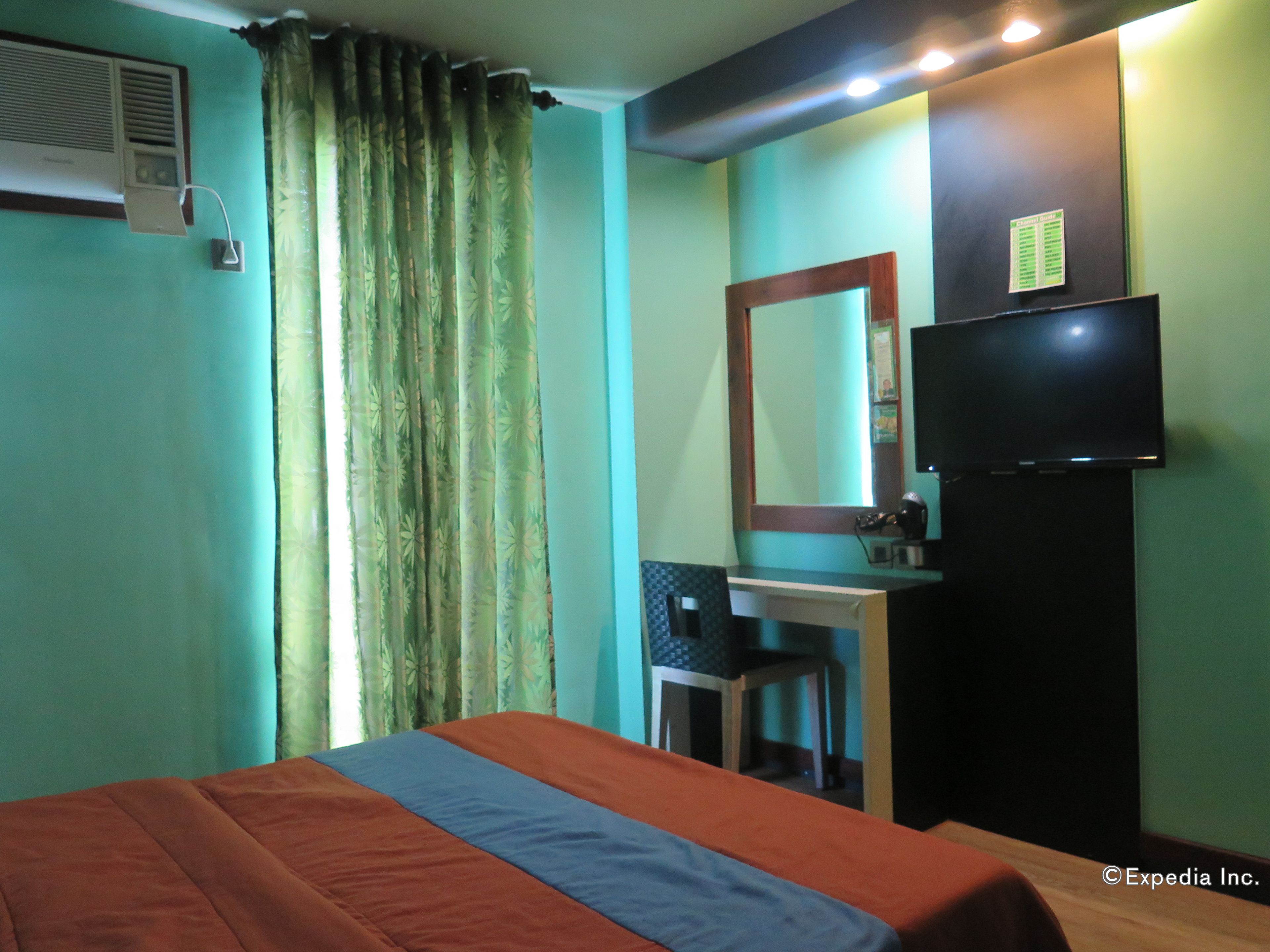 A hotel room with a bed, a desk, a chair, a TV, and a window with curtains.