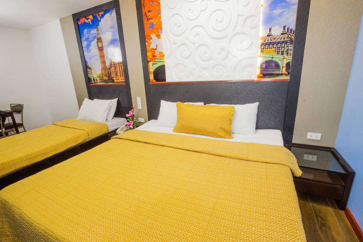Une chambre d’hôtel avec deux lits, chacun recouvert d’une couvre-lit à motifs jaunes et agrémenté d’oreillers blancs. Un panneau décoratif mural représente une vue sur la ville.