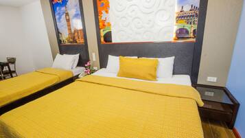 Quarto de hotel com duas camas, cada uma com colcha amarela estampada e almofadas brancas. Há um painel decorativo com imagem de uma paisagem urbana.