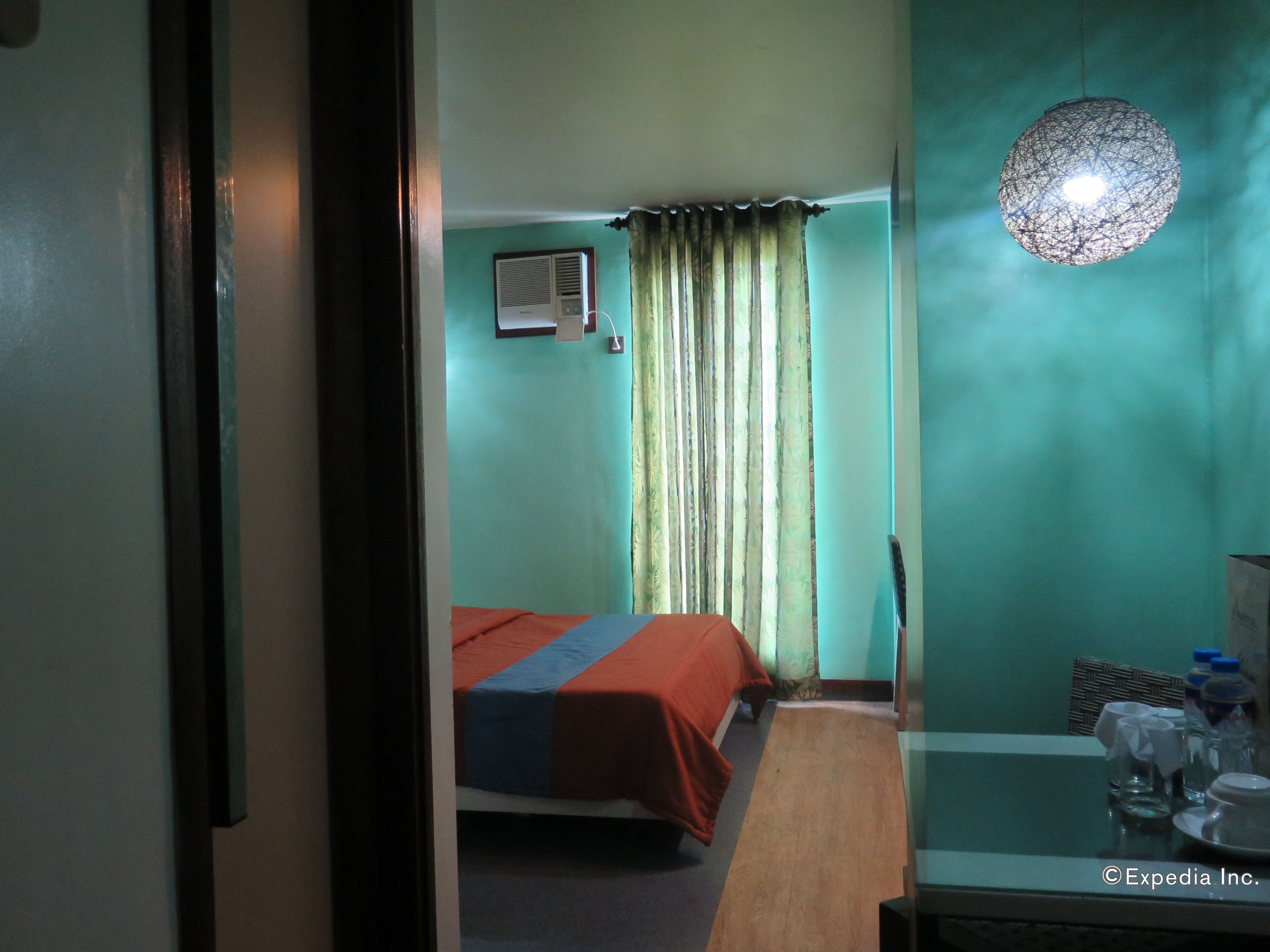 A hotel room with a bed, a table with a glass top, and a hanging light fixture.