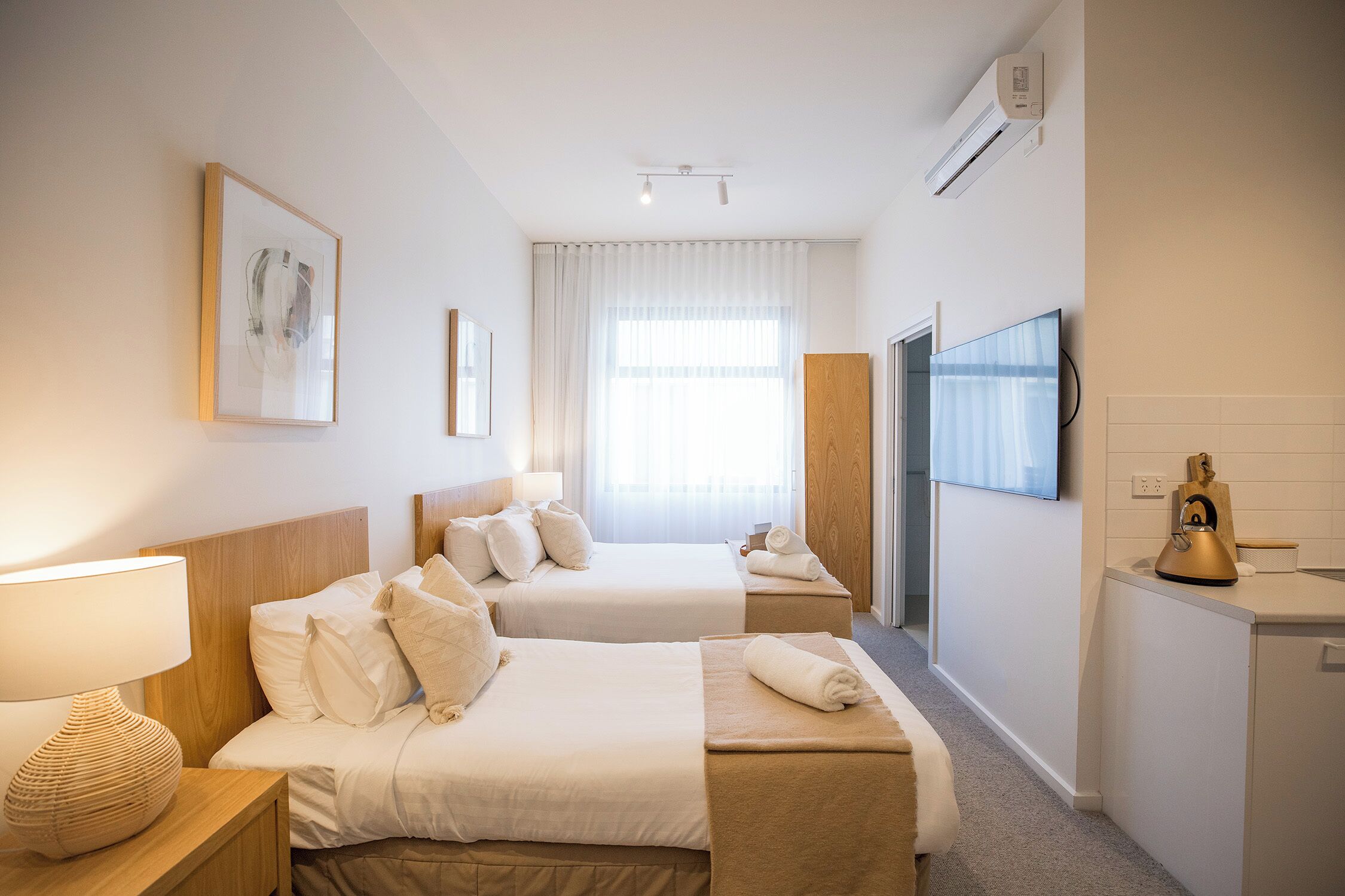 A hotel room with two beds, a TV, a minibar, and a window with curtains.