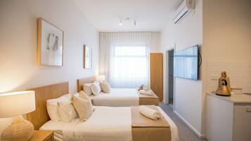A hotel room with two beds, a TV, a minibar, and a window with curtains.