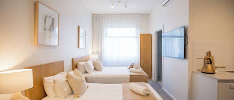 A hotel room with two beds, a TV, a minibar, and a window with curtains.
