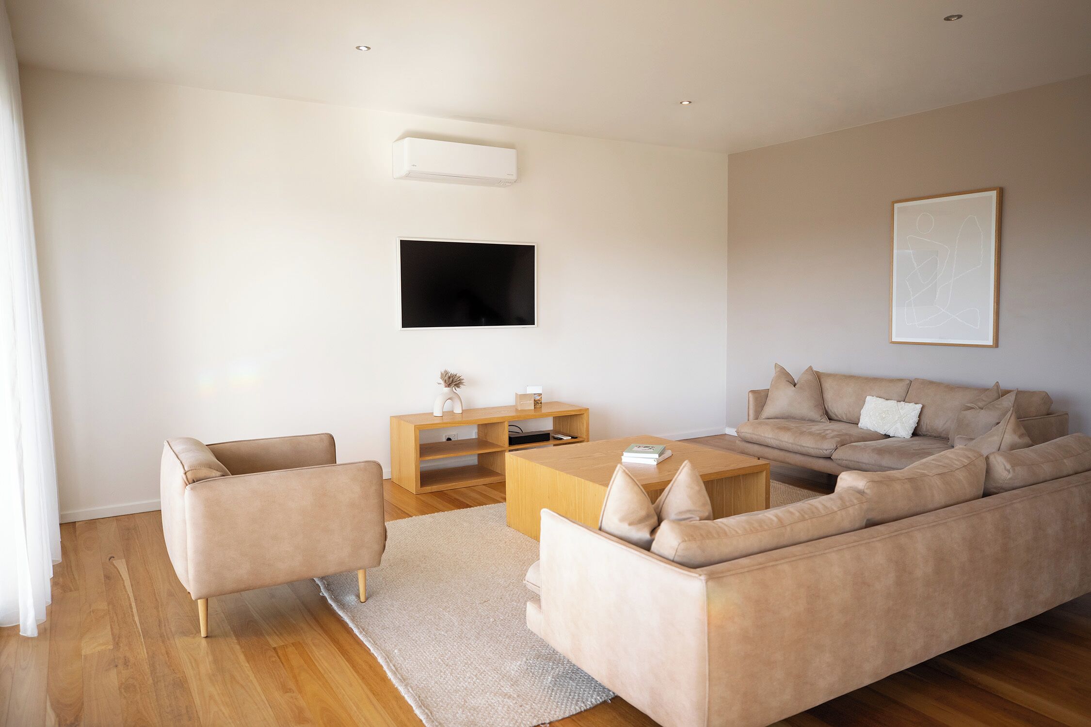 A modern living room with a sofa, armchair, coffee table, TV, and artwork on the wall.