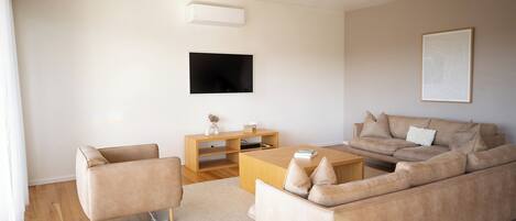 A modern living room with a sofa, armchair, coffee table, TV, and artwork on the wall.