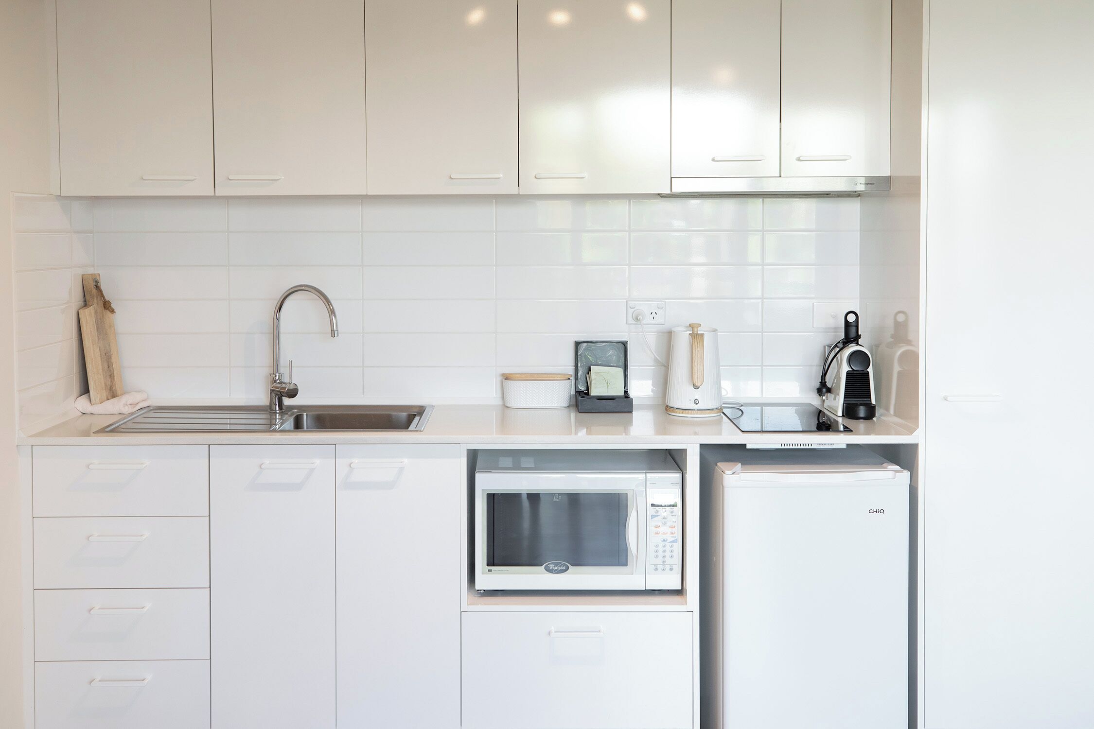 Una cocina moderna con armarios blancos, microondas, cafetera y refrigerador.