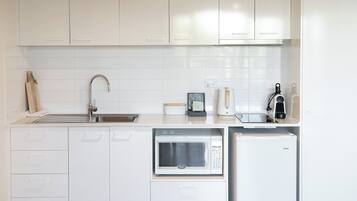 Una cocina moderna con armarios blancos, microondas, cafetera y refrigerador.