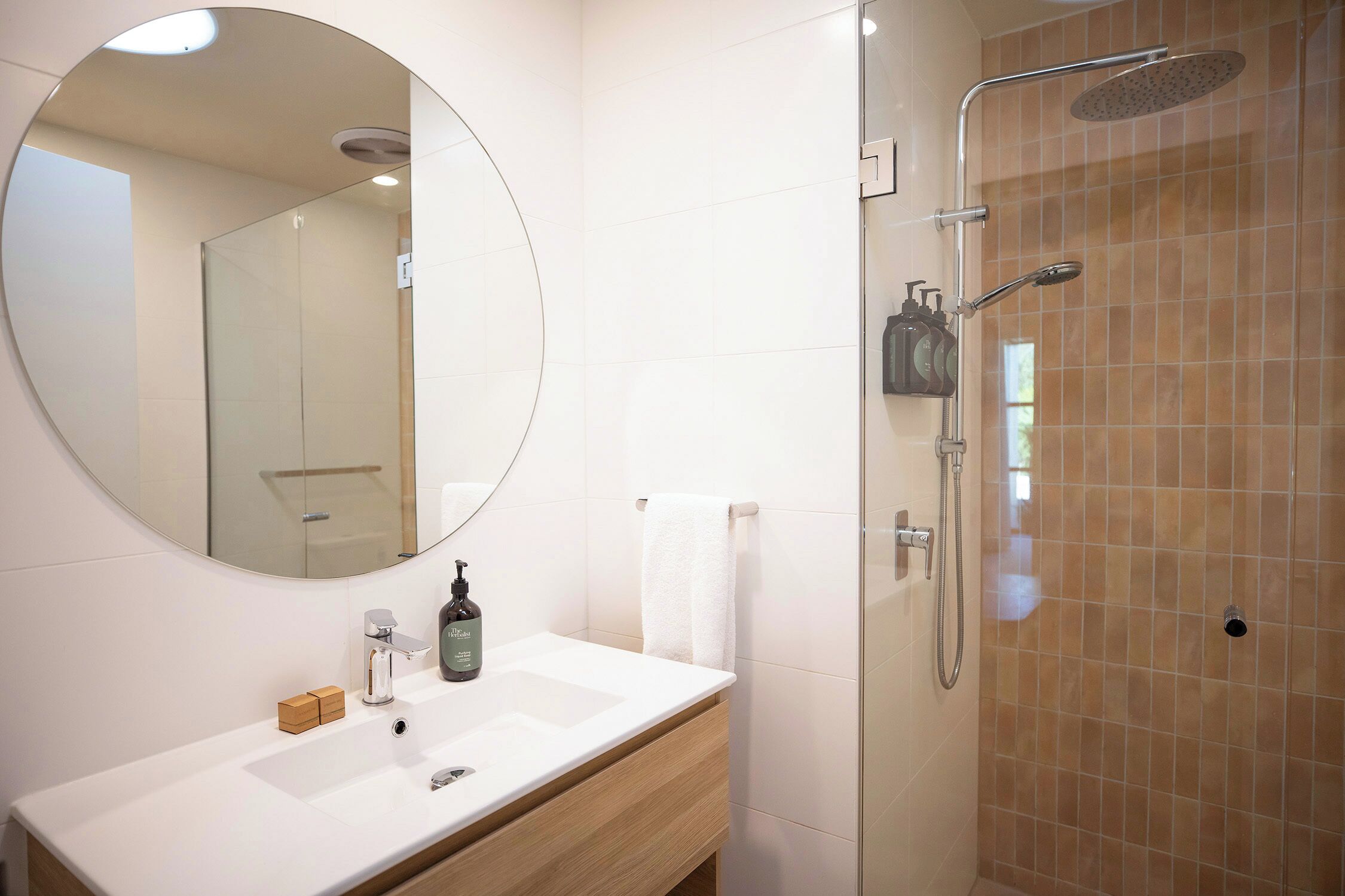 A bathroom with a round mirror, a sink, a handheld showerhead, and a towel rack.