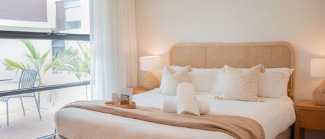 Una habitación de hotel con una cama grande, un balcón con una silla y vistas a palmeras.