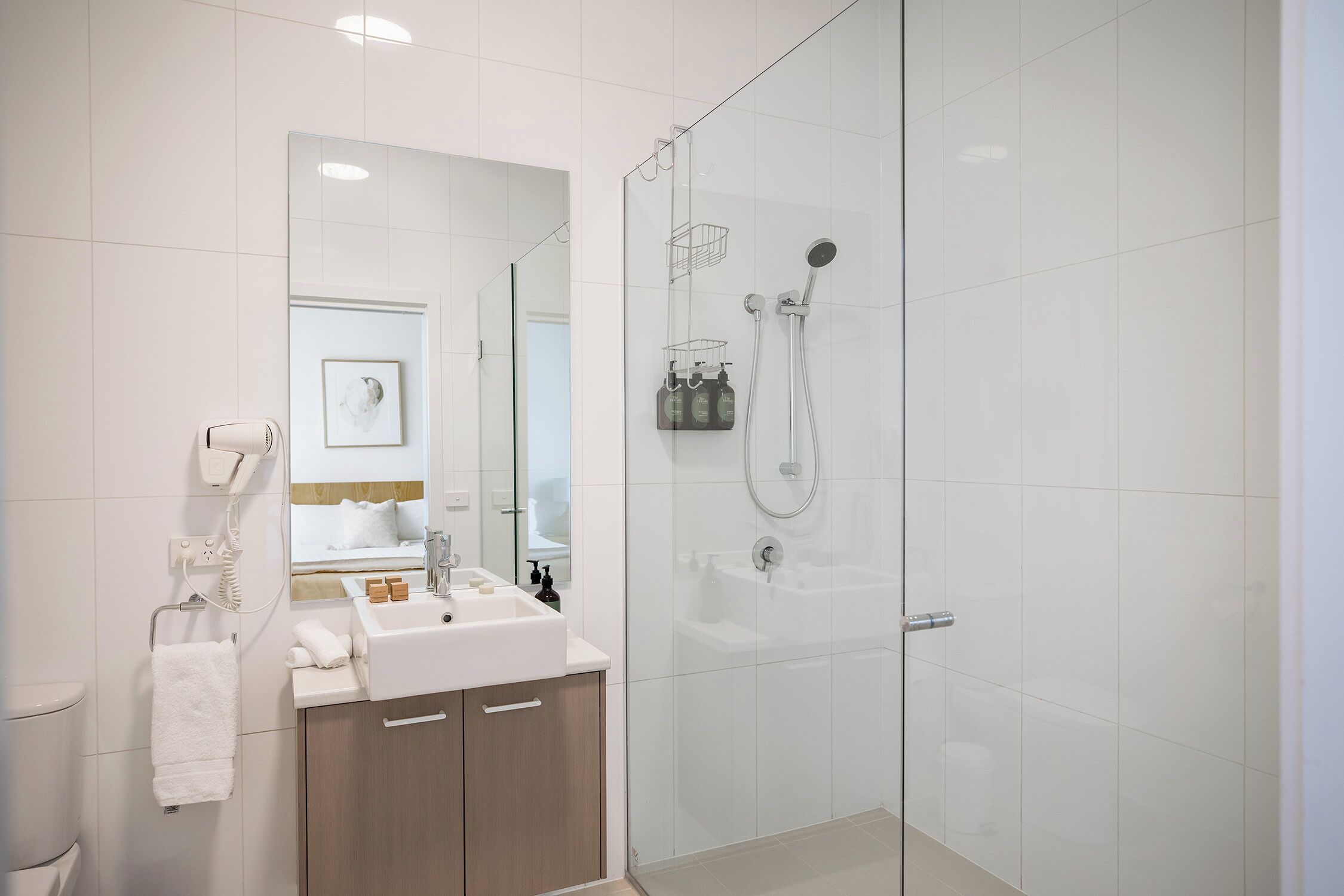 A modern bathroom with a glass-enclosed shower, a sink with toiletries, and a towel hanging on a rack.