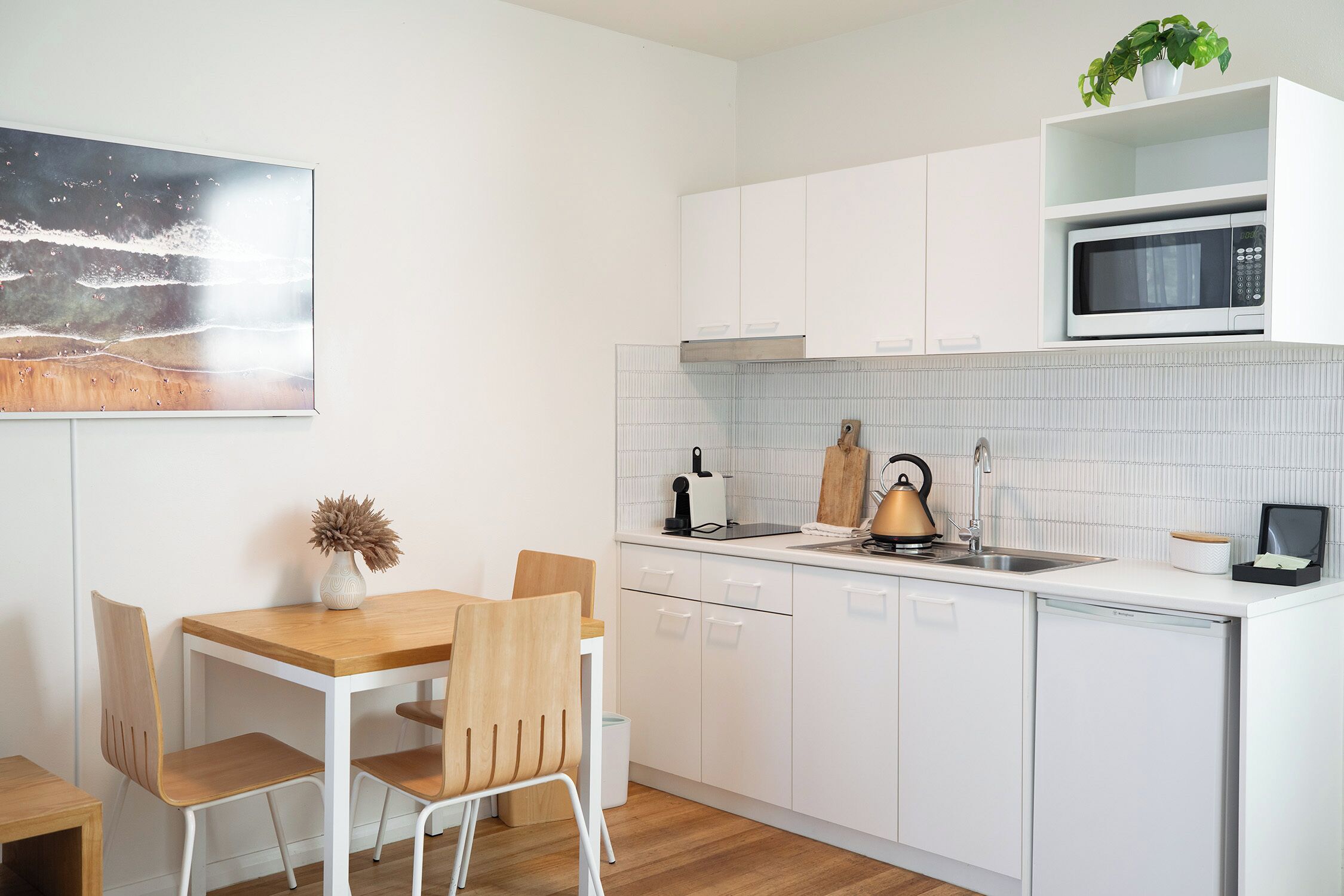 A modern kitchen with white cabinets, a microwave, a sink, and a dining area with a table and chairs.