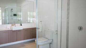 Un baño moderno con ducha de vidrio, lavamanos blanco y retrete.