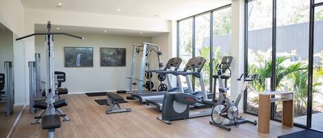 A modern gym with cardio machines, free weights, and a large window offering a view of the outdoors.