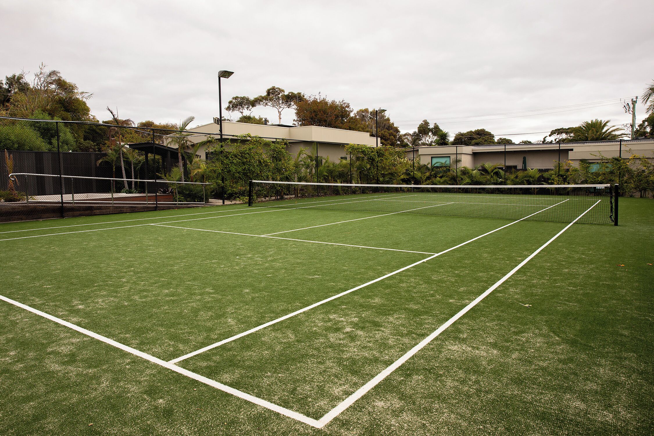A tennis court with a net, surrounded by greenery and buildings.