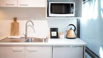 A modern kitchen with a stainless steel sink, a microwave, a kettle, and a cutting board.