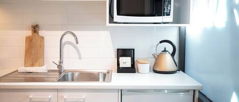 Una cocina moderna con un lavamanos de acero inoxidable, un microondas, una tetera y una tabla de cortar.