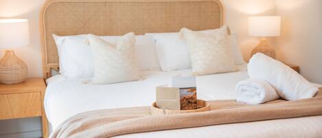 Una cama bien hecha con sábanas blancas, un cabecero color beige y una tarjeta de bienvenida.