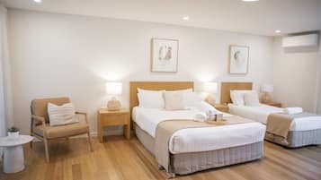 A hotel room with two beds, a chair, a small table, and wall art.