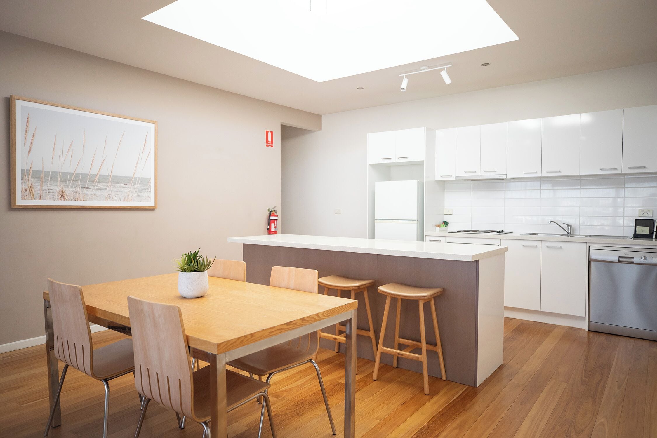 Une cuisine moderne avec des meubles blancs, une table à manger en bois et un petit îlot central doté de tabourets.