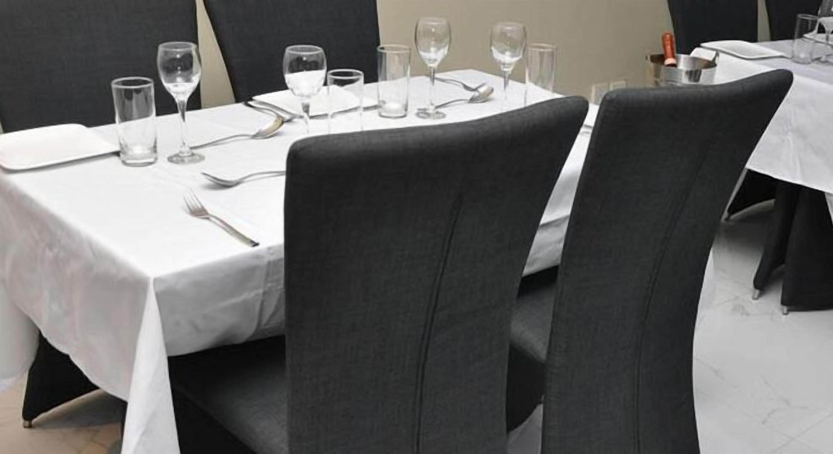 Una mesa de comedor dispuesta con platos, cubiertos y vasos, rodeada de sillas.