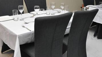 Una mesa de comedor dispuesta con platos, cubiertos y vasos, rodeada de sillas.