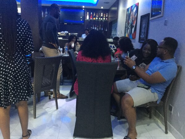 A restaurant interior with tables and chairs, a bar area with bottles, and framed pictures on the walls. - Tudor House Hotel (Lekki)