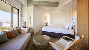 Una habitación de hotel moderna con una cama grande, un sofá, un sillón de mimbre y una mesa de centro de vidrio.