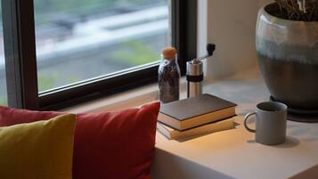 A window view of a road, a potted plant, a book, a coffee mug, and a pepper grinder on a windowsill.